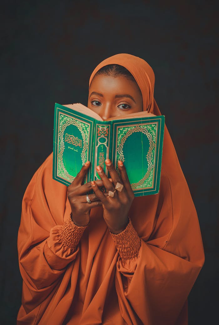 A woman in an orange hijab holds a holy book, showcasing devotion and tradition.