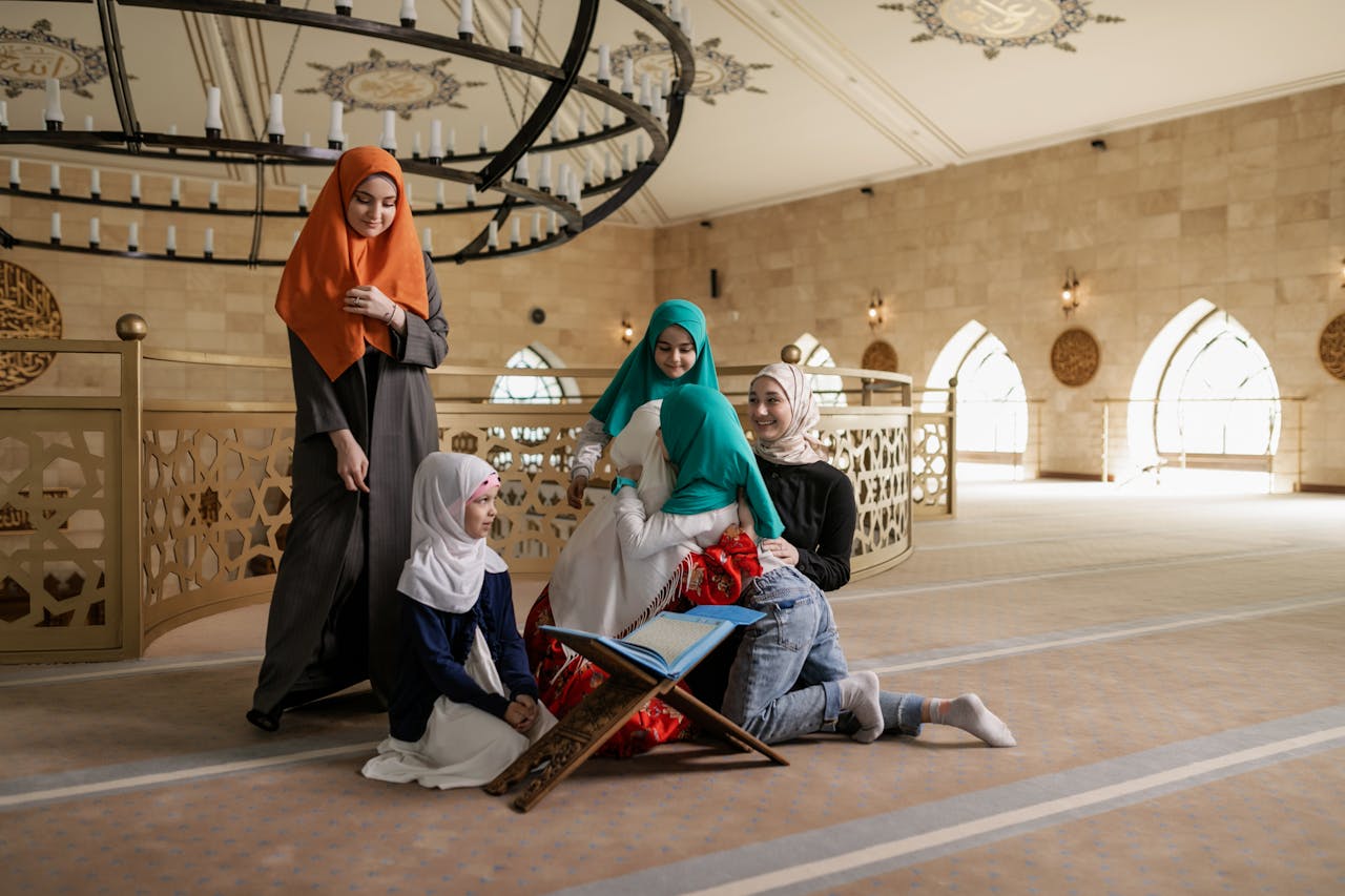 A group of women in hijabs reading the Quran inside a beautifully lit mosque.