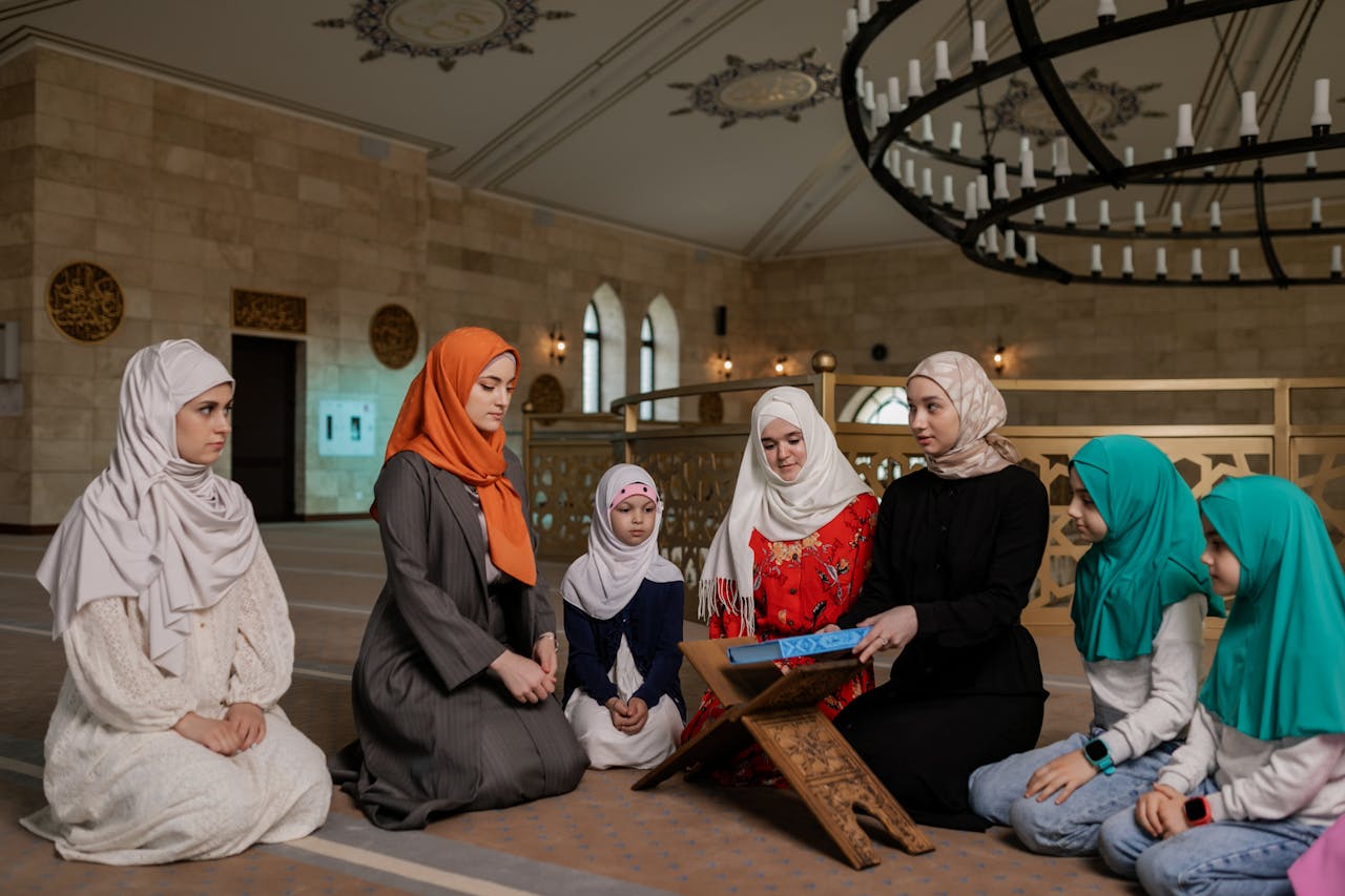 Women and children wearing headscarves praying inside a mosque for religious gathering.